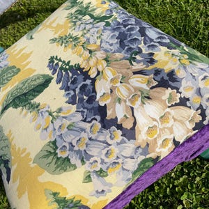 May include: A turquoise chair with a floral patterned cushion. The cushion has a purple velvet trim and features a floral pattern with yellow, white, and blue flowers.
