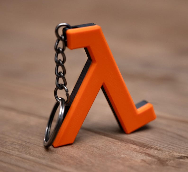 May include: A bright orange Lambda symbol keyring with a black border. The keyring is attached to a silver chain and a silver ring. The Lambda symbol is made of a solid material and is set against a wooden background.