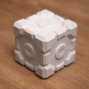 May include: White cube-shaped object with a circular design on the top and a heart-shaped design on each side.