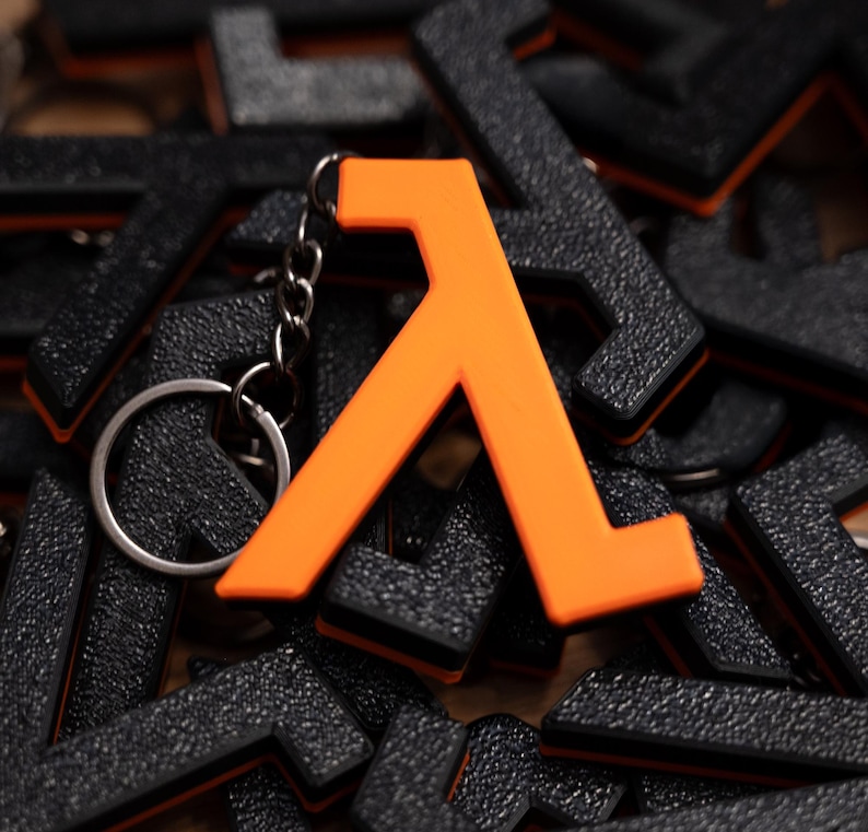 May include: An orange lambda symbol keyring with a silver ring. The lambda symbol is prominent, set against a backdrop of many black lambda keyrings. These keyrings are a gaming accessory.