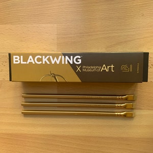 May include: A box of 12 gold pencils with the text "Blackwing x Philadelphia Museum of Art" on the box. The pencils have a gold finish and a black eraser.