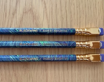 May include: Three black and green marbled pencils with gold accents and purple erasers. The pencils are labeled "Blackwing x Robert Brighton".