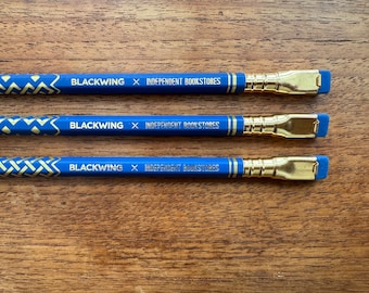 May include: Three blue pencils with gold accents and a geometric pattern. The pencils have a gold eraser and the text "BLACKWING x INDEPENDENT BOOKSTORES" printed on them.