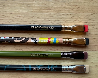 May include: Four black pencils with different colored and patterned barrels. The pencils are labeled "Blackwing 20", "Blackwing 557", "Blackwing 17", and "Blackwing 2".