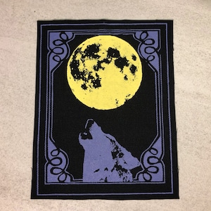 May include: A black fabric patch with a design of a howling wolf beneath a yellow full moon. The image is framed by a purple border with decorative swirls. The patch is rectangular.