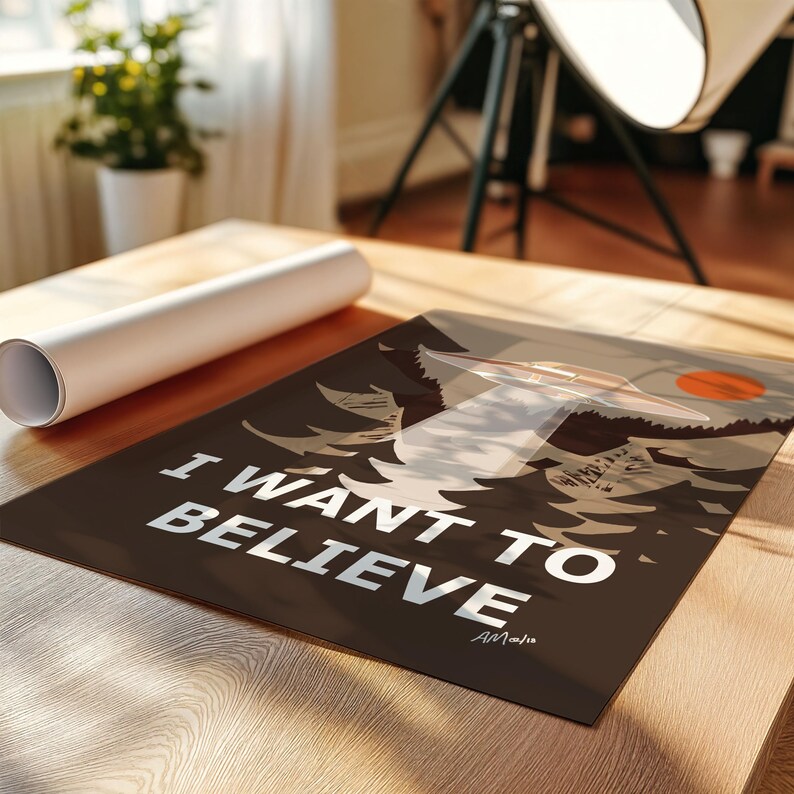 Op de afbeelding: Een bruine poster met de tekst "I WANT TO BELIEVE" in witte letters. De poster toont een zwart-witte illustratie van een UFO die over een bos vliegt.