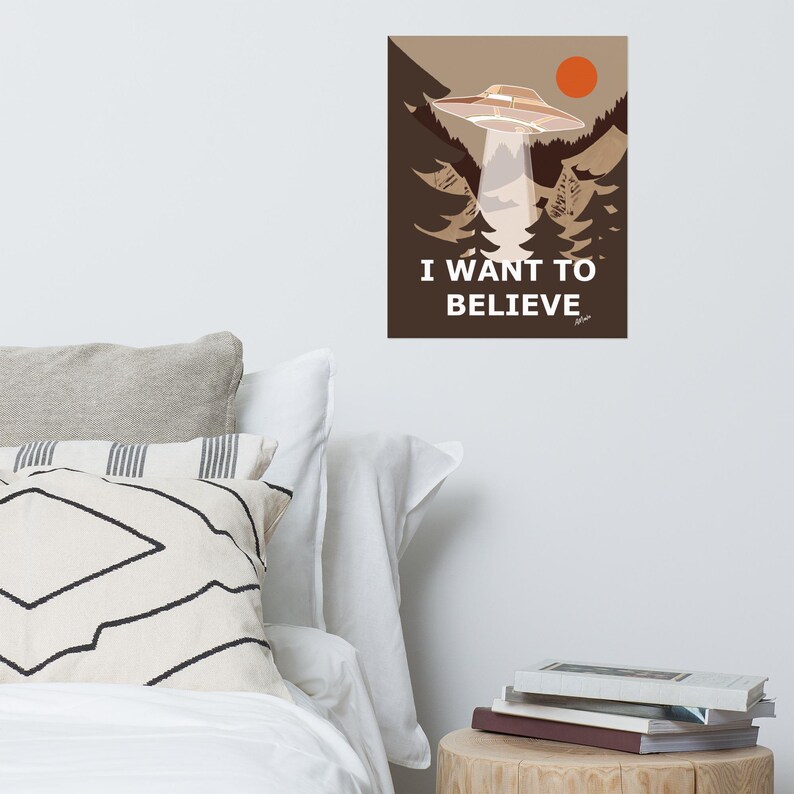 Op de afbeelding: Een bruine en witte poster met een UFO die over een bos vliegt. De poster zegt "Ik wil geloven".