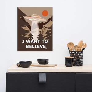 Op de afbeelding: Een bruine en witte poster met een UFO die over een bos vliegt. De poster zegt "I WANT TO BELIEVE".