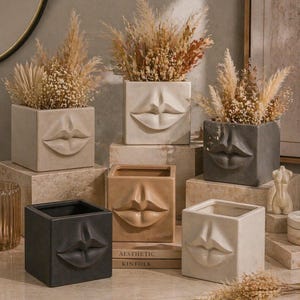 Può includere: Una collezione di fioriere quadrate in ceramica in varie tonalità neutre, ognuna con un design a labbra scolpite. Le fioriere sono riempite con erbe ornamentali essiccate. L'arrangiamento include libri con il testo "Aesthetic Kinfolk".