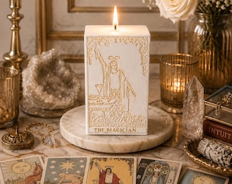 Puede incluir: Una vela blanca encendida con un diseño dorado en relieve de la carta del tarot "El Mago". La vela está sobre un posavasos de mármol, rodeada de cartas del tarot, flores y otros objetos decorativos. El tema es espiritual y místico.
