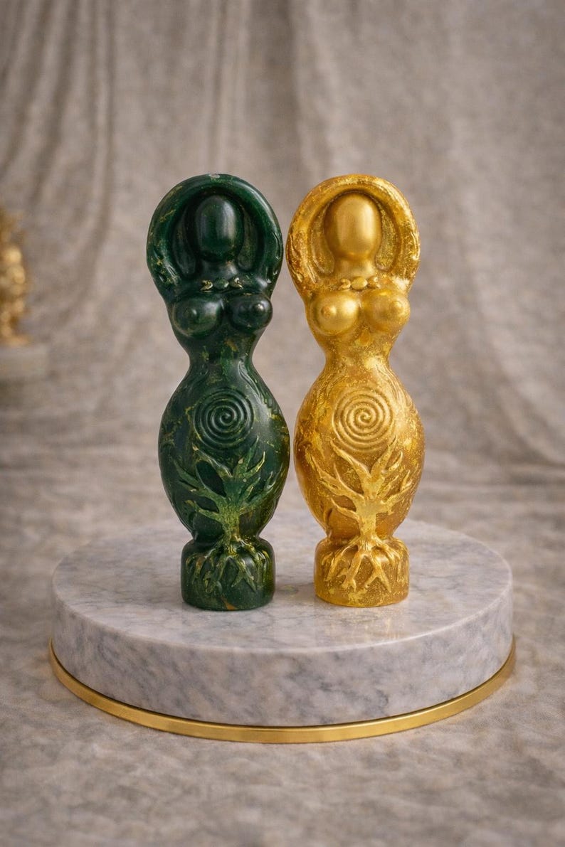 May include: Two goddess statues, one green and one gold, stand on a marble pedestal with a gold trim. The statues have a tree of life design on the lower half and a spiral design on the upper half. The statues are approximately 6 inches tall.