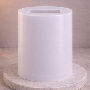 Puede incluir: Un recipiente cil&iacute;ndrico blanco con un acabado liso y mate y una abertura rectangular en la parte superior. El objeto presenta un dise&ntilde;o vertical limpio con una base plana y lados uniformes, ofreciendo una forma simple y funcional.