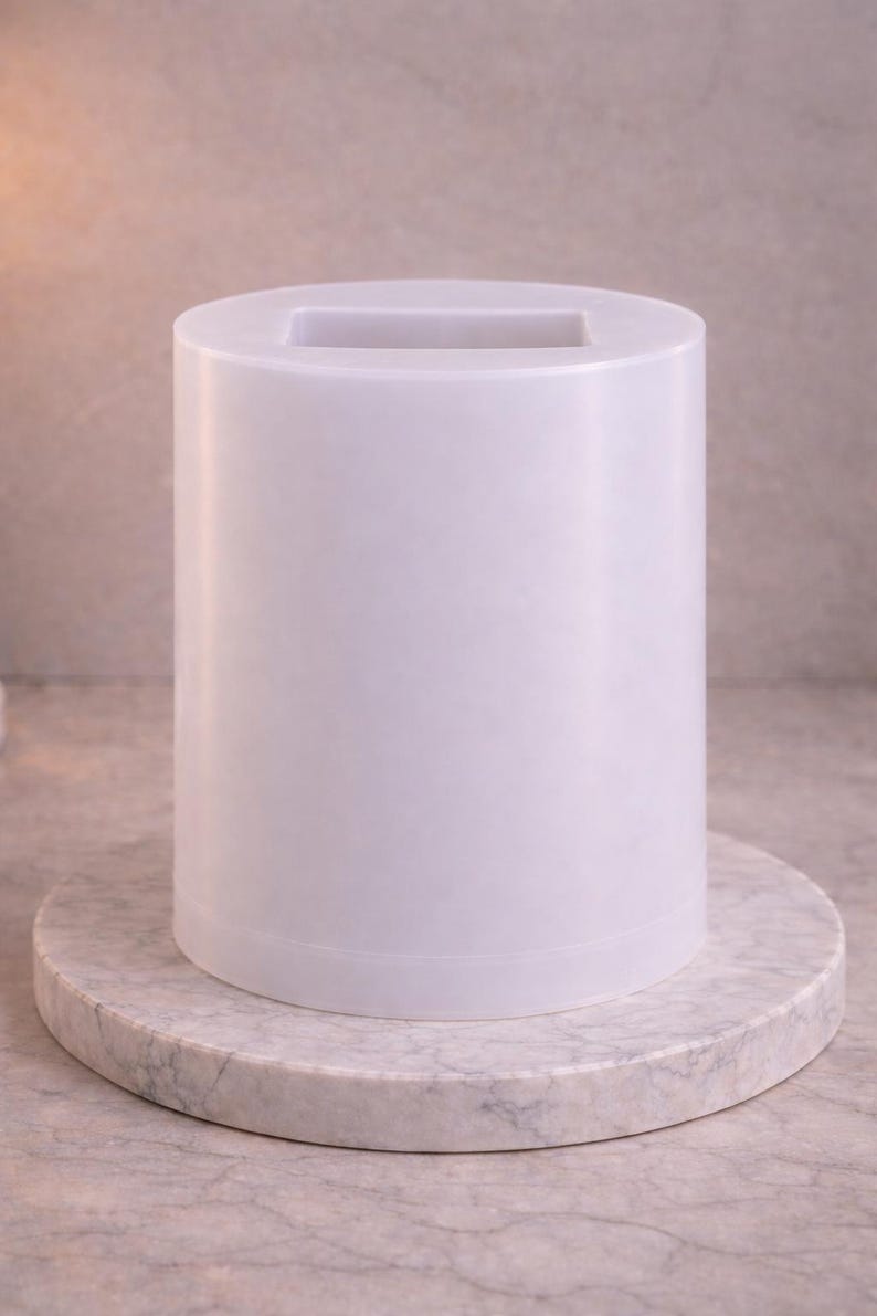 Puede incluir: Un recipiente cil&iacute;ndrico blanco con un acabado liso y mate y una abertura rectangular en la parte superior. El objeto presenta un dise&ntilde;o vertical limpio con una base plana y lados uniformes, ofreciendo una forma simple y funcional.