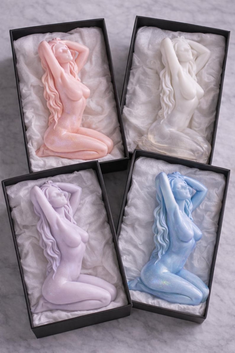 Puede incluir: Cuatro velas decorativas con forma de figuras arrodilladas de cabello largo y fluido, presentadas cada una en una caja rectangular negra forrada con papel de seda blanco. Las velas tienen acabados en colores rosa pastel, blanco, lavanda y azul claro.