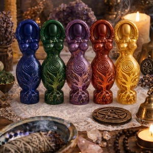 May include: Five colorful goddess statues in blue, green, purple, red, and gold, each with a spiral design on the torso and a tree of life on the base. The statues are arranged on a lace cloth, with candles and other spiritual items in the background.
