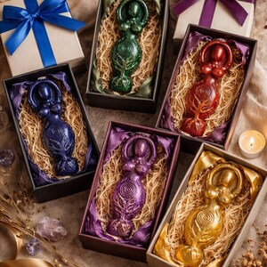 May include: Six goddess figurines in various colors, including green, blue, red, purple, and gold, are presented in decorative boxes with straw and ribbon. The boxes are arranged with gift boxes and a lit candle, creating a mystical theme.