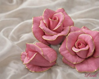 May include: Three pink roses with gold trim, resting on a soft, white fabric. The roses have multiple layers of petals and a delicate appearance. The text "Pink roses" is at the bottom right.