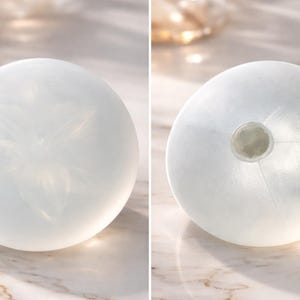 May include: Two white, spherical decorative objects. One has a floral design etched on its surface. The other has a circular opening at the top. Both are translucent and appear to be made of glass or a similar material. The objects are likely vases or decorative pieces.
