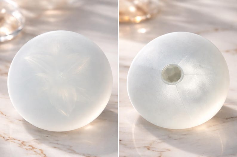 May include: Two white, spherical decorative objects. One has a floral design etched on its surface. The other has a circular opening at the top. Both are translucent and appear to be made of glass or a similar material. The objects are likely vases or decorative pieces.