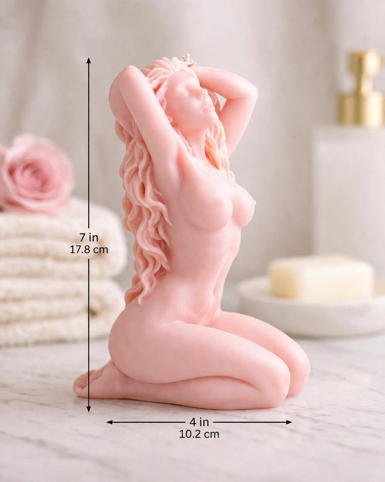 Puede incluir: Una vela de color rosa p&aacute;lido con forma de figura arrodillada con el cabello largo y ondulado y los brazos levantados sobre la cabeza. La figura mide 17,8 cm de alto y 10,2 cm de ancho, seg&uacute;n indican las l&iacute;neas de cota negras en la imagen.
