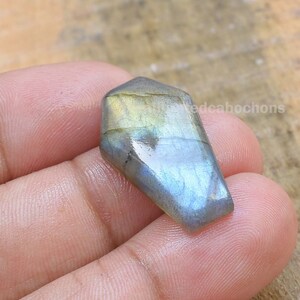 May include: A blue-green labradorite gemstone cabochon with iridescent flashes of color. The cabochon is cut in a teardrop shape and has a smooth, polished surface.