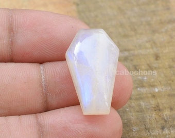 May include: A white moonstone cabochon cut in the shape of a coffin. The stone has a blue iridescent sheen.