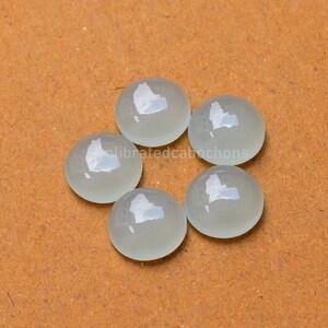 May include: Six round, white, translucent cabochons on a brown surface.