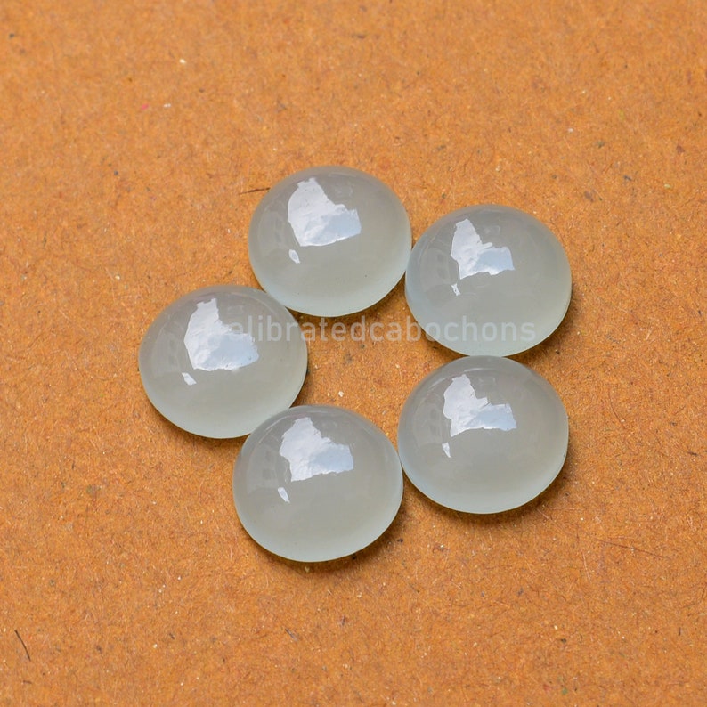 May include: Six round, white, translucent cabochons on a brown surface.