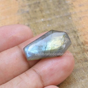 May include: A teardrop-shaped, iridescent labradorite gemstone cabochon with a smooth, polished surface. The stone displays a range of colors, including blue, green, and gold.
