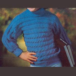 Pode incluir: Um suéter azul de malha com um padrão de trança. O suéter tem gola alta e mangas compridas.