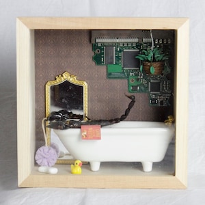 May include: A whimsical shadow box scene featuring a white bathtub with a scorpion inside. A small mirror, a yellow rubber duck, and a miniature book are also present. The background includes a patterned wallpaper and a circuit board.