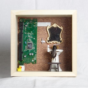 May include: A shadow box art piece featuring a miniature bathroom scene. A circuit board is mounted on the left, with a small sink, mirror, and a figure in the center. The background is a patterned wallpaper, and the frame is made of light wood.