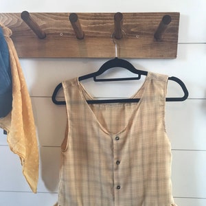 May include: A sleeveless, yellow and brown plaid top with a ruffled hem and button closure.
