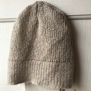 May include: A beige knitted beanie with a ribbed texture. The beanie has a folded brim.