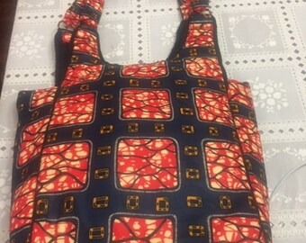 Pode incluir: Uma bolsa tote vermelha, laranja e azul com um padrão geométrico. A bolsa tem duas alças e um fecho de correr.