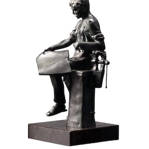 May include: A bronze sculpture of a person seated, working on a piece of paper. The figure is dressed in clothing and seated on a chair-like structure. The sculpture is mounted on a dark, rectangular base.
