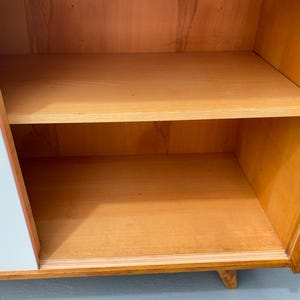 Peut inclure: Une armoire bleu clair avec un int&eacute;rieur en bois. L'armoire a deux &eacute;tag&egrave;res et une seule porte avec une poign&eacute;e blanche.