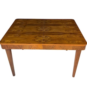 May include: A rectangular wooden table with a warm brown finish and a unique wood grain pattern. The table has four angled legs and a two-piece tabletop design. The table measures approximately 102 cm long and 76 cm wide.