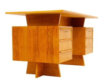 May include: A mid-century modern desk made of light wood with a rectangular top and two sets of drawers. The desk has a unique design with a raised platform in the center and a lower base with a cross-shaped support.