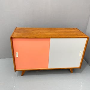 Peut inclure: Un buffet moderne du milieu du si&egrave;cle avec deux portes coulissantes. Le buffet est en bois avec une finition brun clair. Les portes sont peintes dans un sch&eacute;ma de couleurs rose clair et blanc.