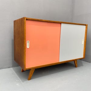 Peut inclure: Un buffet moderne du milieu du si&egrave;cle avec des portes coulissantes. Le buffet est en bois avec une finition brun clair. Les portes sont peintes dans un sch&eacute;ma de couleurs rose clair et blanc.