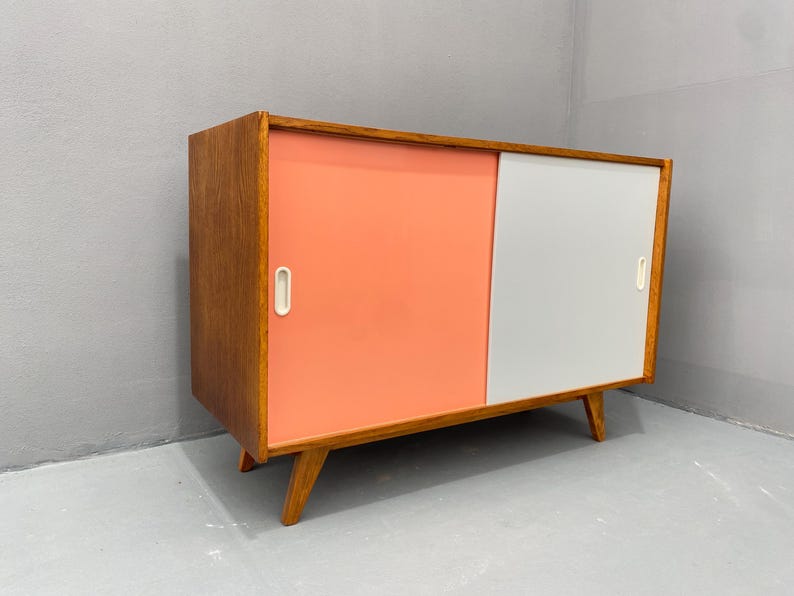 Peut inclure: Un buffet moderne du milieu du si&egrave;cle avec des portes coulissantes. Le buffet est en bois avec une finition brun clair. Les portes sont peintes dans un sch&eacute;ma de couleurs rose clair et blanc.