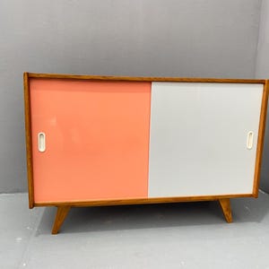 Peut inclure: Un buffet moderne du milieu du si&egrave;cle avec deux portes coulissantes. Le buffet est en bois et a une finition en bois clair. Les portes sont peintes dans un sch&eacute;ma de couleurs rose clair et blanc.