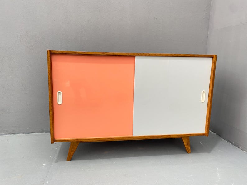 Peut inclure: Un buffet moderne du milieu du si&egrave;cle avec deux portes coulissantes. Le buffet est en bois et a une finition en bois clair. Les portes sont peintes dans un sch&eacute;ma de couleurs rose clair et blanc.