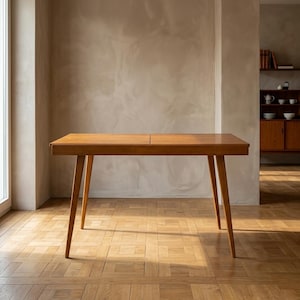 May include: A rectangular wooden dining table with a smooth, medium-brown finish. The table features a flat top surface with a visible seam in the center and four tapered, angled legs that extend outward from the corners to provide support.