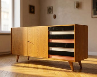 May include: A mid-century modern wooden cabinet with a light brown finish. The cabinet has two doors on the left and a section with black, white, and pink horizontal stripes on the right. The cabinet is elevated on angled wooden legs.