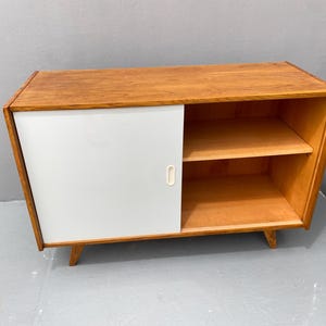 Peut inclure: Un meuble en bois avec une porte coulissante et deux &eacute;tag&egrave;res. Le meuble est peint en blanc et a une finition en bois clair.