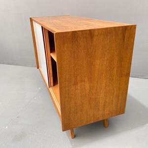 Peut inclure: Un meuble en bois de style moderne du milieu du si&egrave;cle avec des portes coulissantes. Le meuble est en bois clair et l'int&eacute;rieur est blanc. Le meuble a deux &eacute;tag&egrave;res et repose sur quatre pieds.