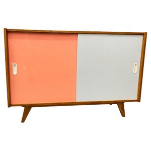 Peut inclure: Un buffet moderne du milieu du si&egrave;cle avec deux portes coulissantes. La porte de gauche est rose p&acirc;le et la porte de droite est blanche. Le buffet a un cadre en bois et quatre pieds.