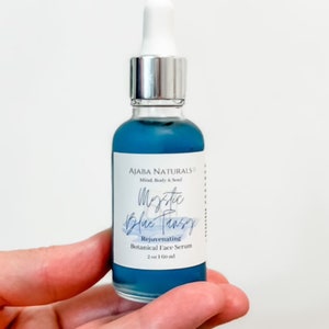 May include: A blue glass bottle with a silver dropper top. The label reads "AJABA NATURALS Mind, Body & Soul Mystic Blue Pansy Rejuvenating Botanical Face Serum 2 oz 160 ml".